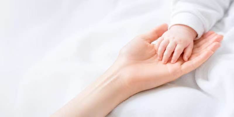 A newborn's hand resting in an adult's palm